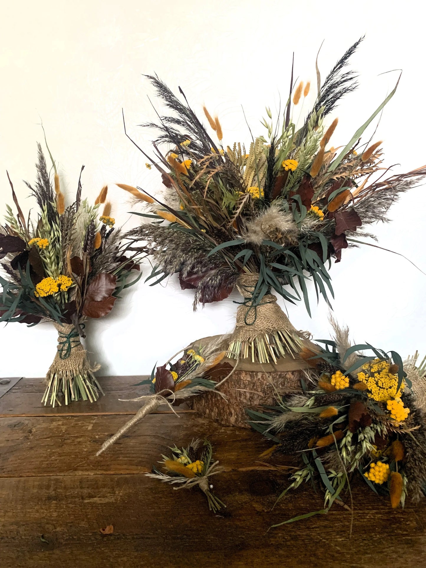 Brown & Ochre dried flower bouquet for bride and bridesmaids, wedding heart wand for Flower Girl and a matching buttonhole displayed on a wooden table with log slice.