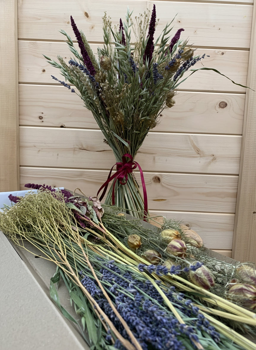 Bouquet of dried lavender, flowers and grasses tied with a burgundy bow. And a cardboard box with a selection of same dried flowers, the contents of letterbox gift. Displayed on a wooden surface
