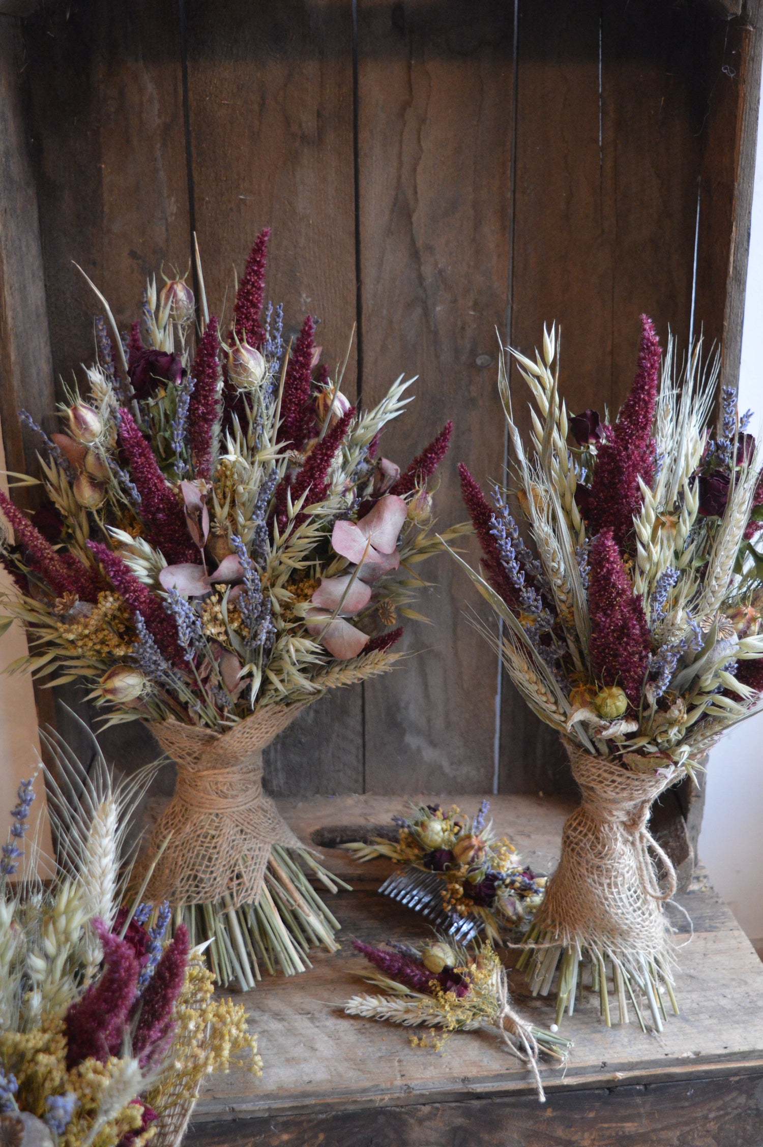 A brides and bridesmaid dried flower bouquet in warm burgundy and greens with lavender. Displayed with a matching dried flower buttonhole and hair comb.