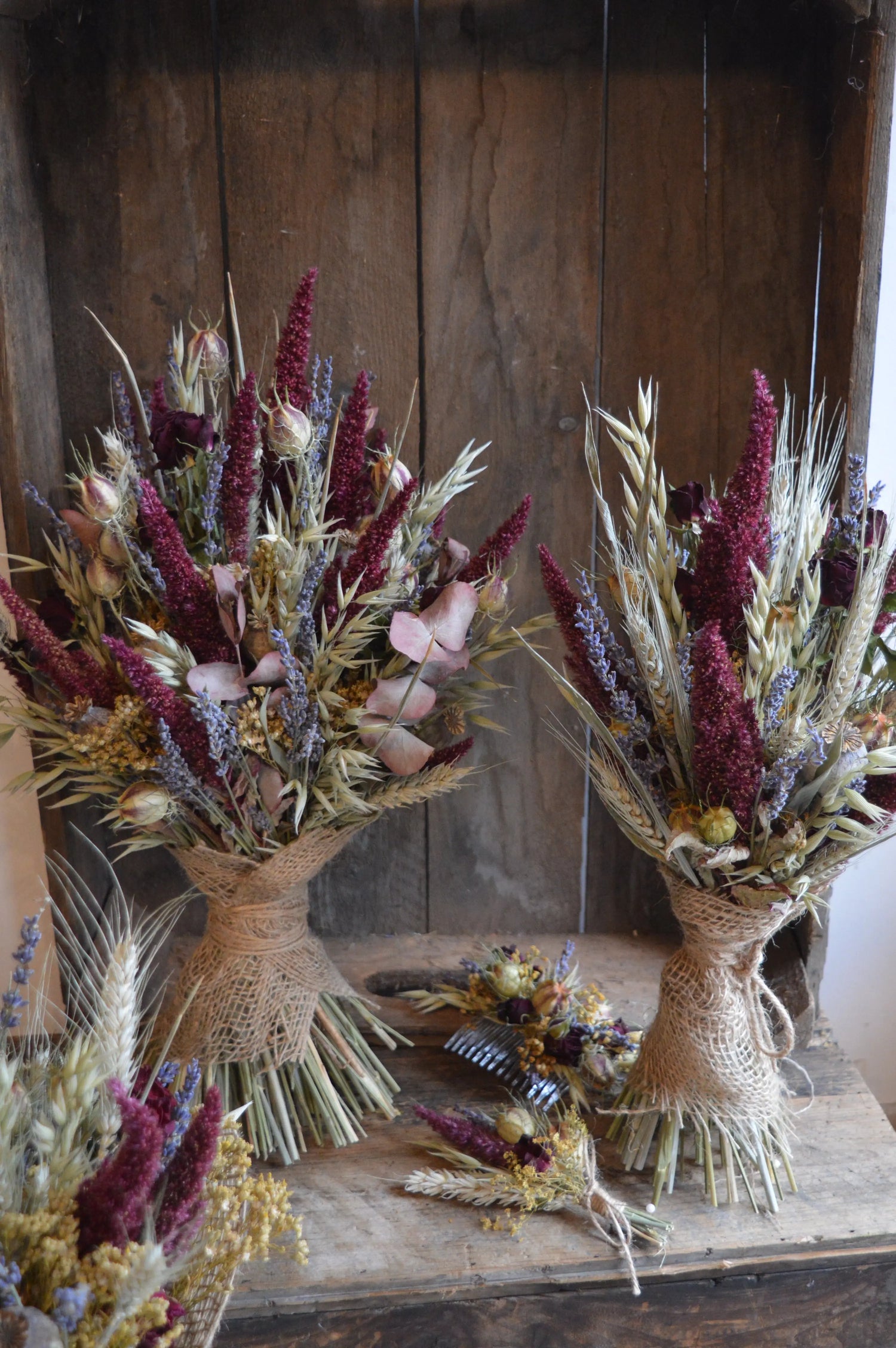 A brides and bridesmaid dried flower bouquet in warm burgundy and greens with lavender. Displayed with a matching dried flower buttonhole and hair comb.