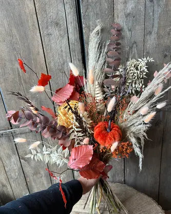 Autumn Bouquet of dried flowers with a velvet pumpkin held against a wooden background