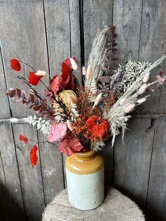 Dried floral arrangement in a stoneware vase against a wooden background