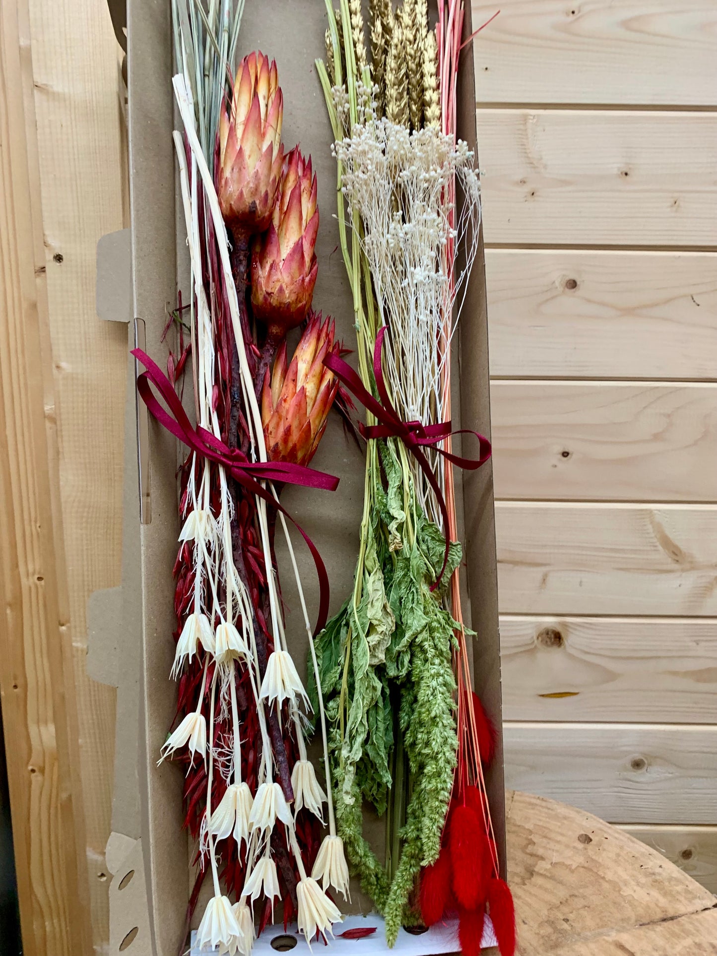 A selection of dried flowers, the contents of the Christmas letterbox gift, in a cardboard box on a wooden surface