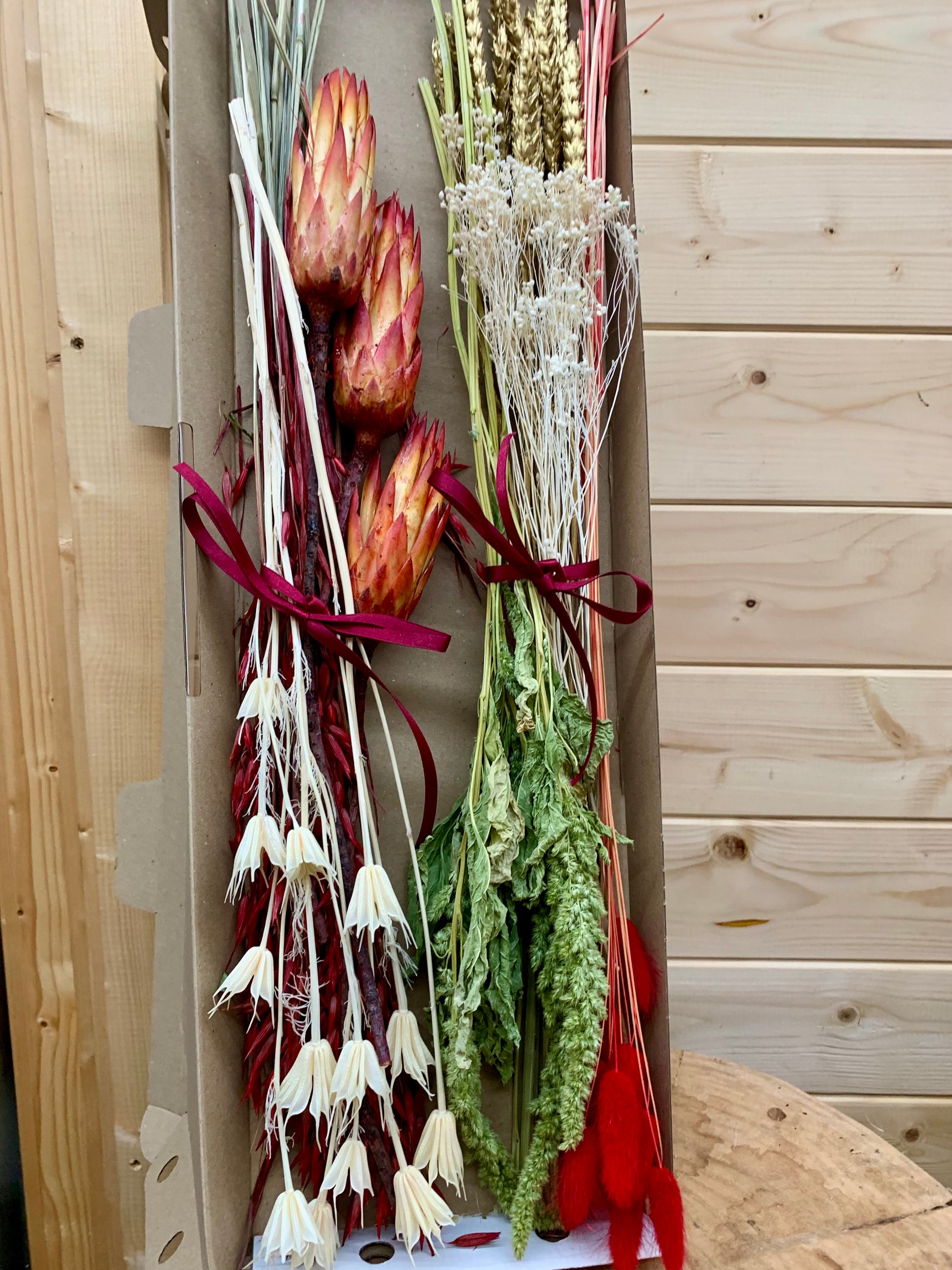 A selection of dried flowers, the contents of the Christmas letterbox gift, in a cardboard box on a wooden surface