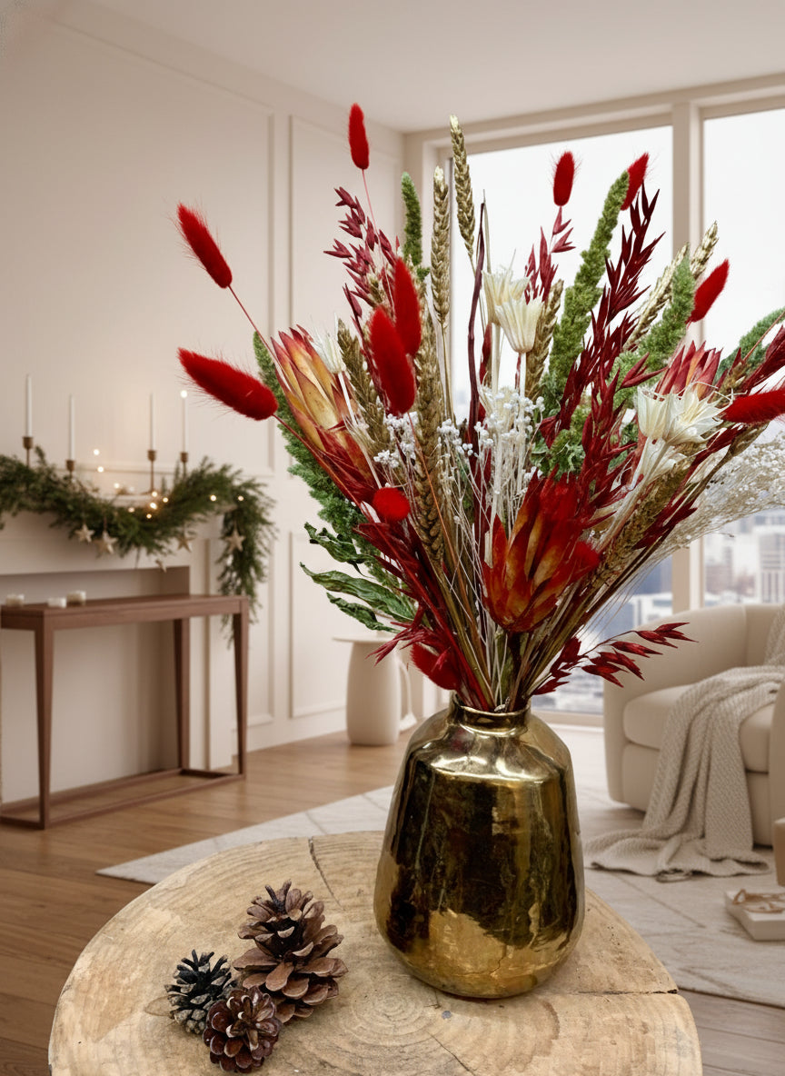 Gold vase with dried flowers and pinecones on a wooden surface against a wooden wall.