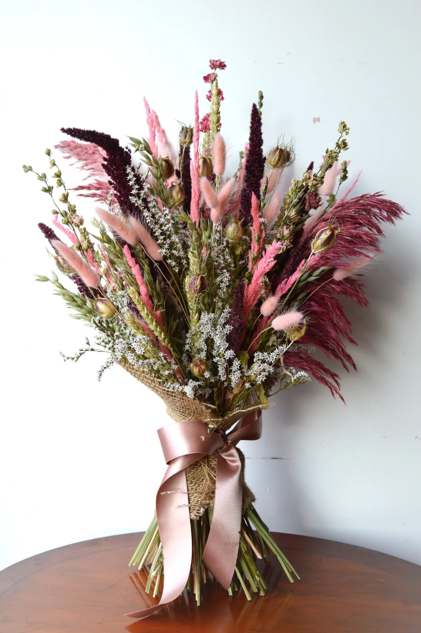 Dusky Pinks Dried Flower Bouquet on a dark wood side table against a white wall