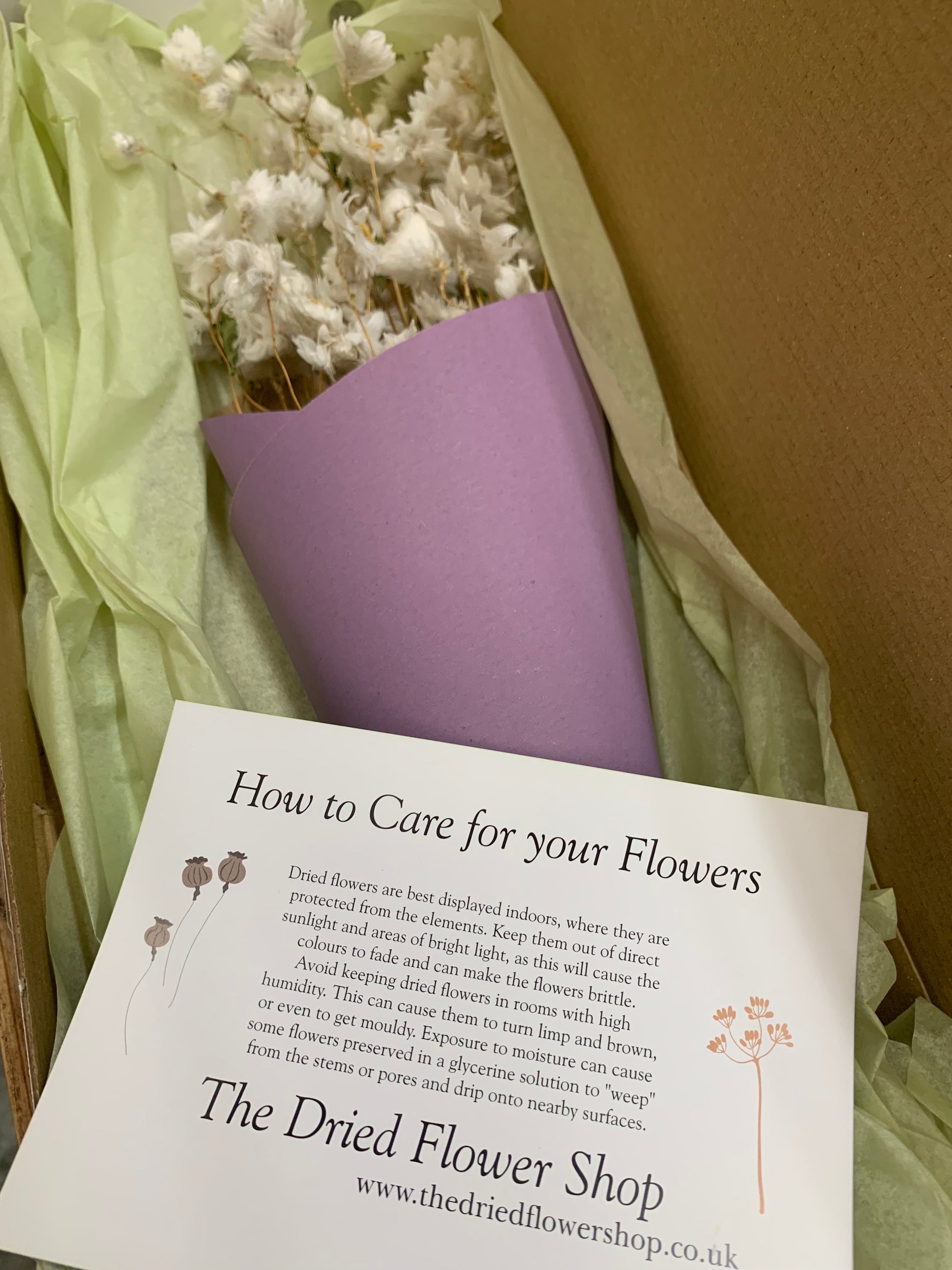 Bouquet of dried flowers with a care guide on a cardboard surface