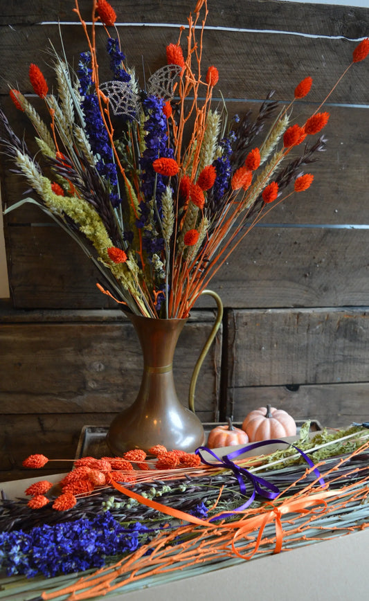 Orange and purple Dried flowers with a bat in a copper jug on a wooden surface with a rustic background