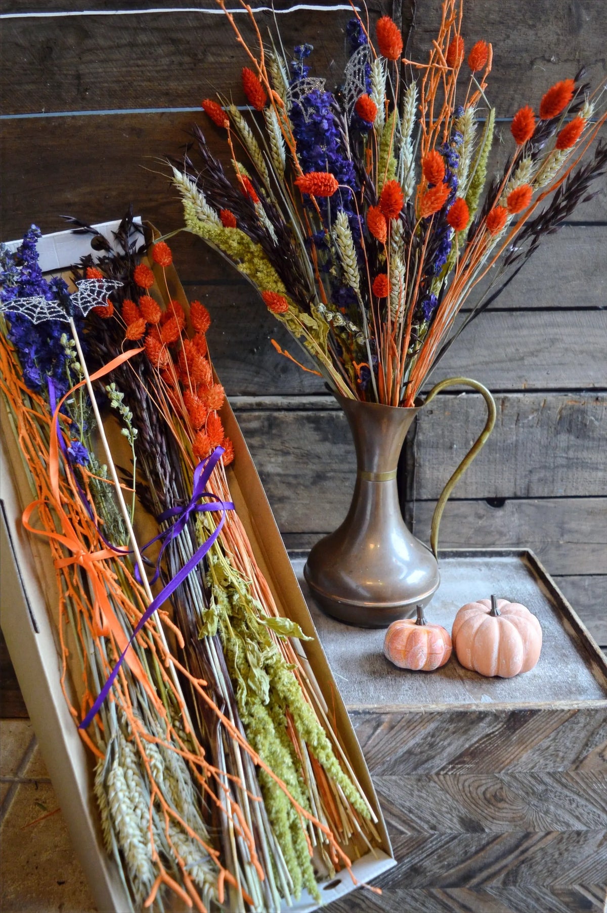Dried floral arrangement for Halloween in a brass jug on a wooden surface with pumpkins.