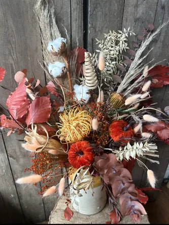 Dried floral arrangement with autumn colours in a white vase against a wooden background