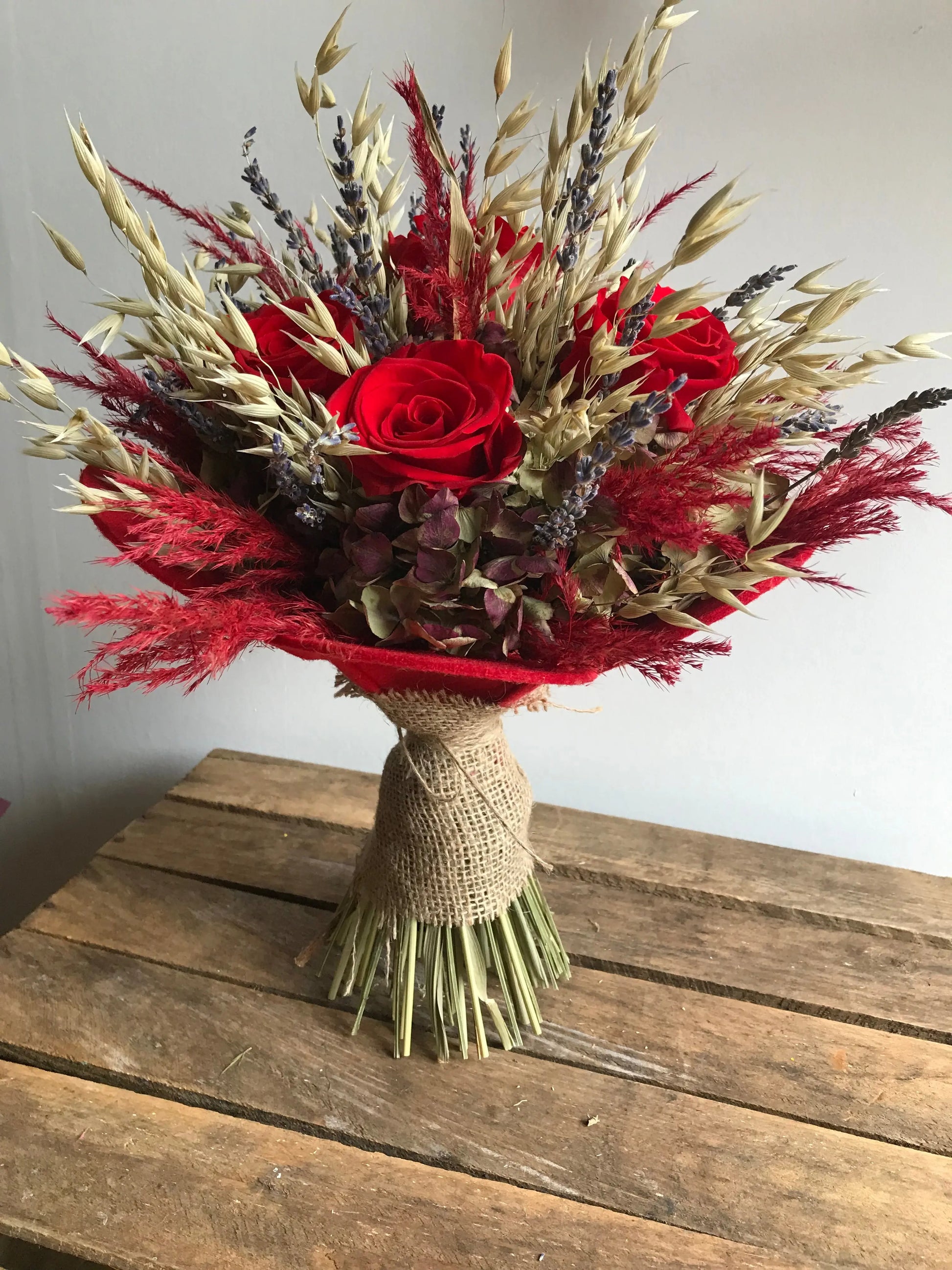 Bouquet of preserved red roses and dried flowers wrapped in hessian on a wooden surface 