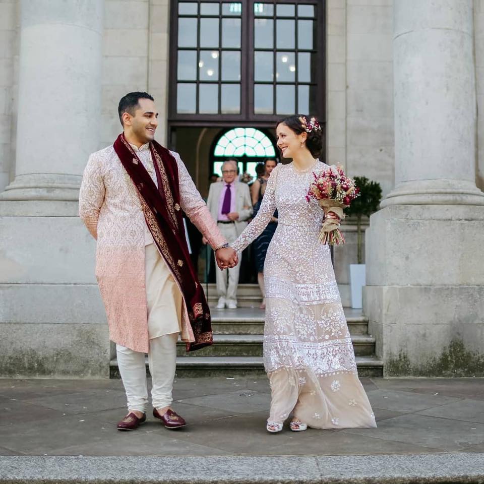 Bride and groom in traditional formal Indiana wedding attire standing in front of a building with columns with the bride holding a dried flower bouquet in in pink and magenta tones with dried babies breath. 