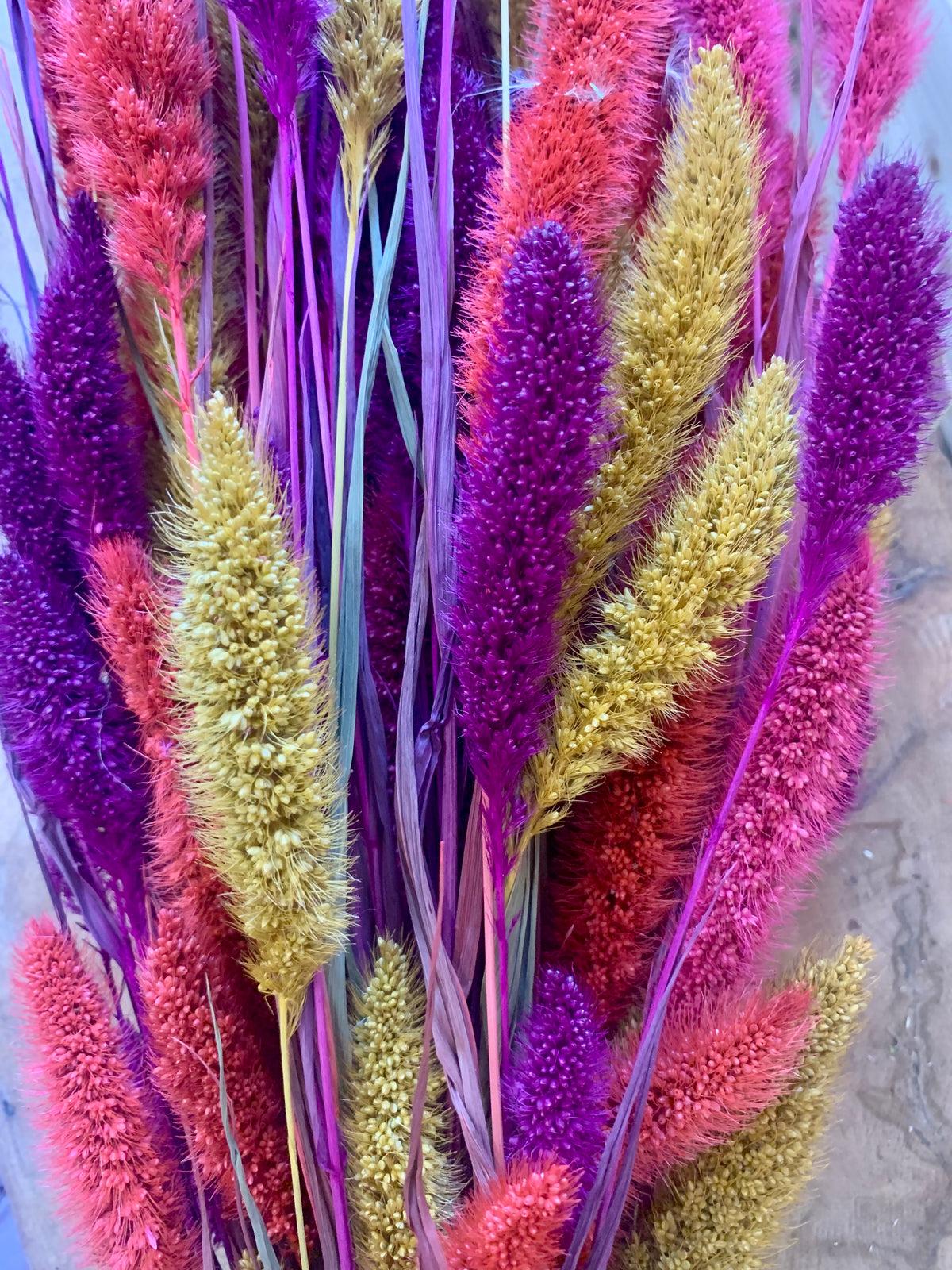 A close-up of a dried floral arrangement featuring vibrant purple, magenta, and golden-yellow ornamental grasses with long, slender stems.