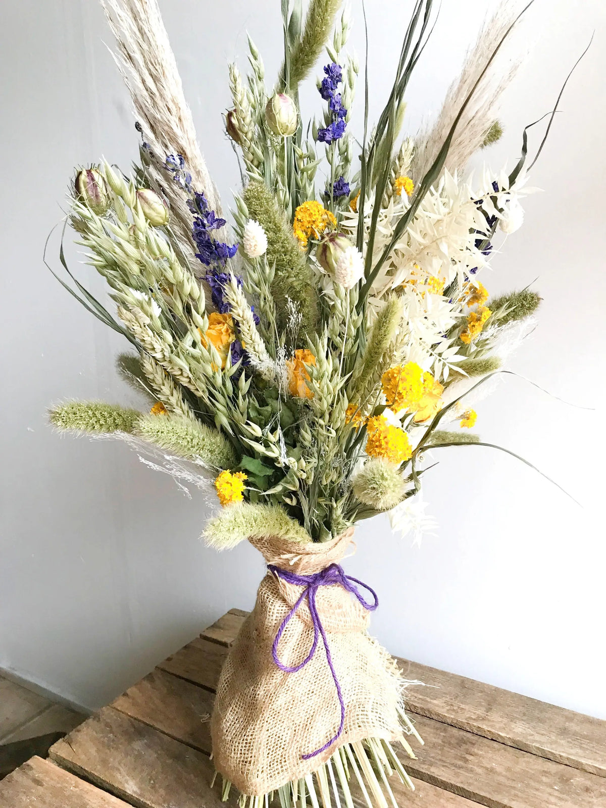 Bouquet of dried flowers in a burlap wrap on a wooden surface with a white background