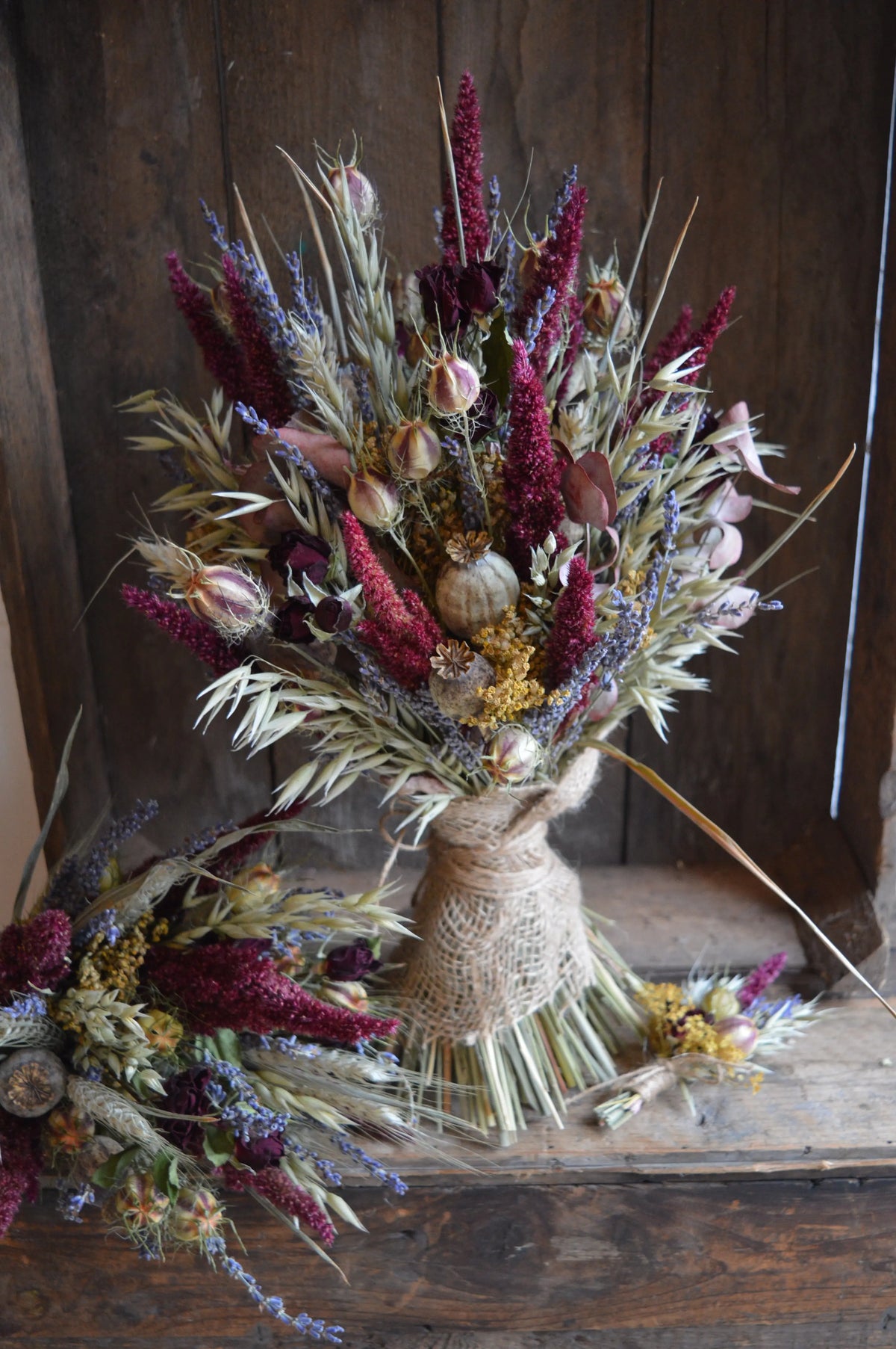 Bouquet of dried flowers in warm winter colours using burgundy amaranthus, love-in-a-mist seed heads, lavender and grasses tied with hessian against a wooden background