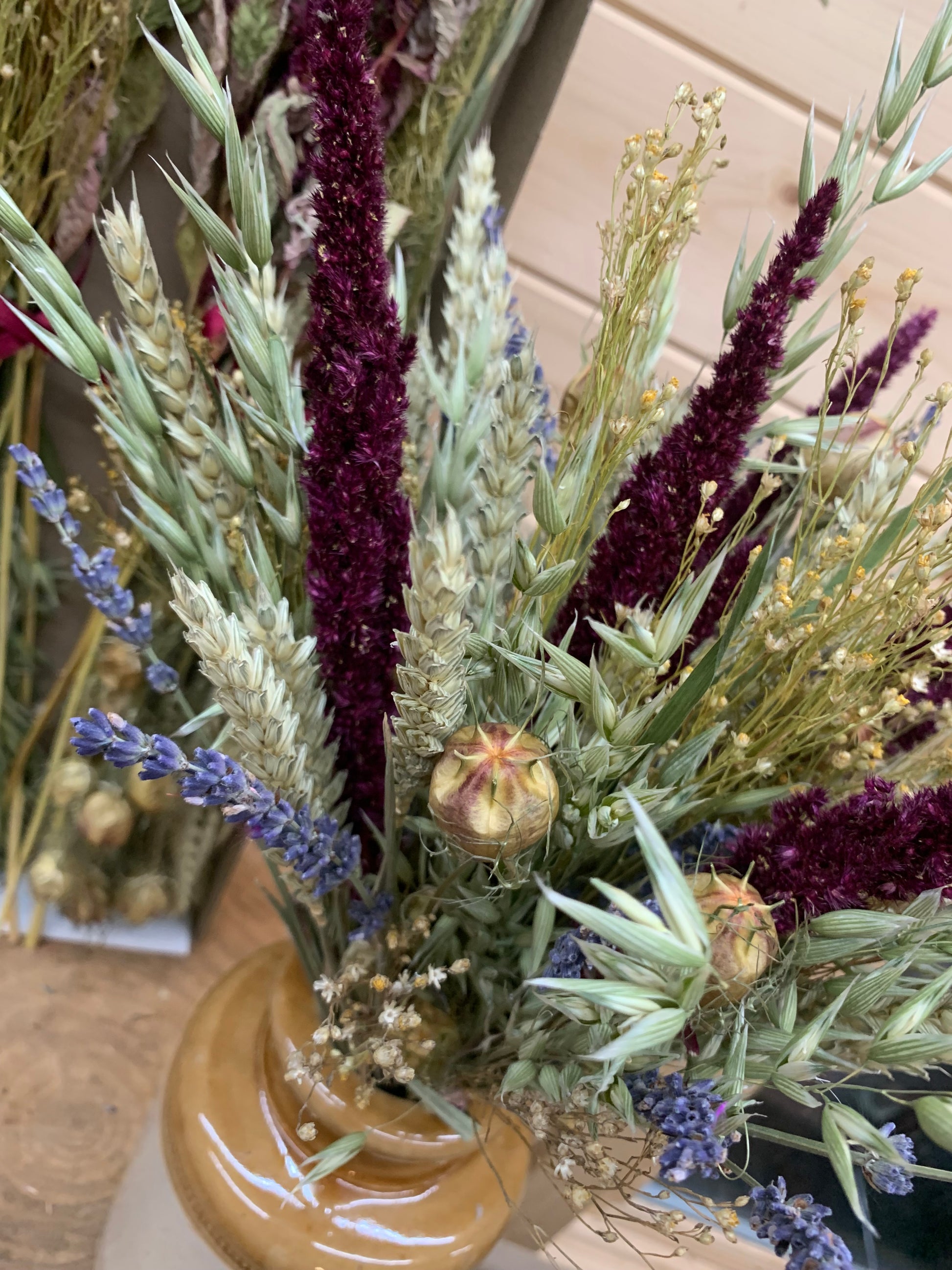 Bouquet of dried flowers and grasses in a brown vase on a wooden surface