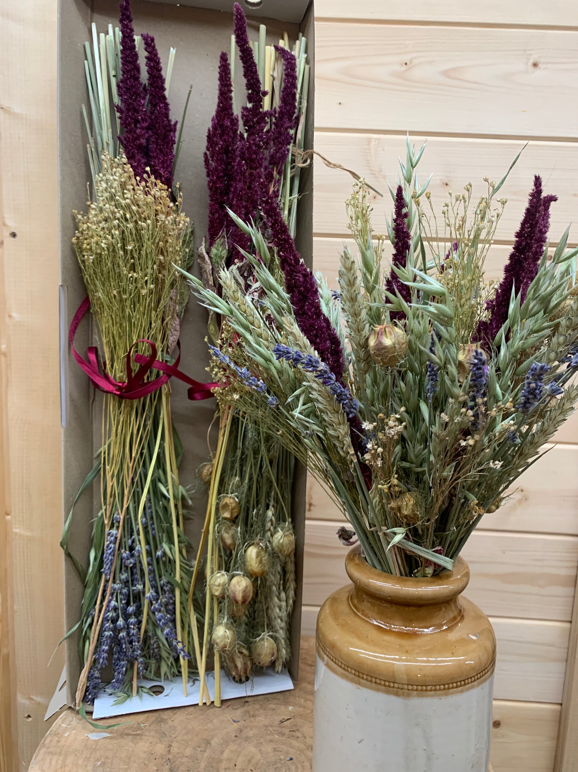 Bouquet of dried lavender and grasses in a stoneware vase on a wooden surface.
